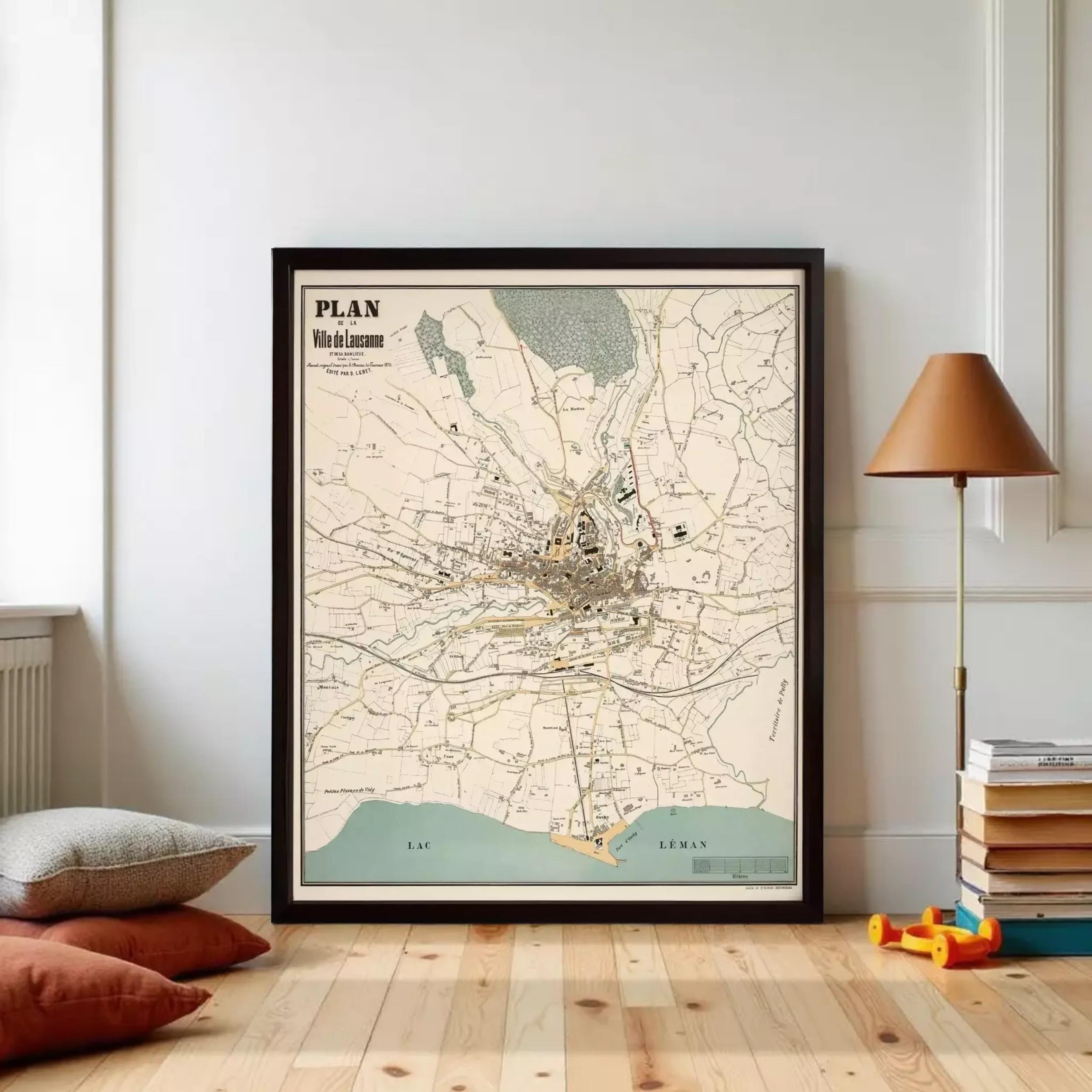 a framed map of a city, with a lamp and a stack of books on the floor in the foreground.