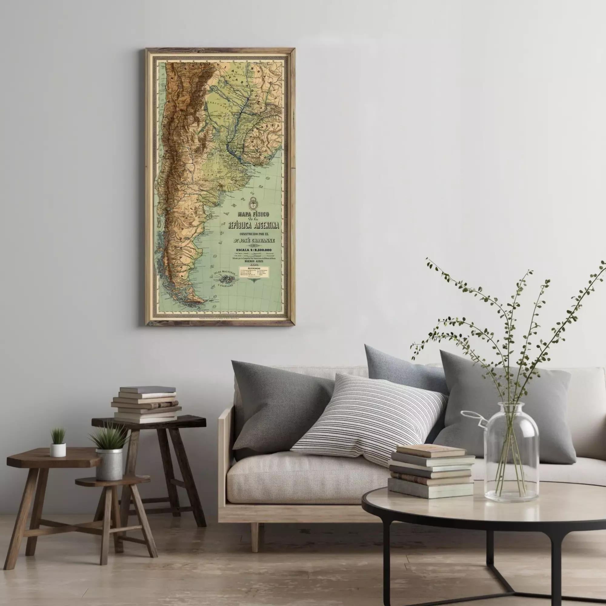 a living room with a large framed map of South America hanging on the wall above a couch with pillows. There are also some books and a vase with flowers on the couch, creating a cozy and inviting atmosphere.