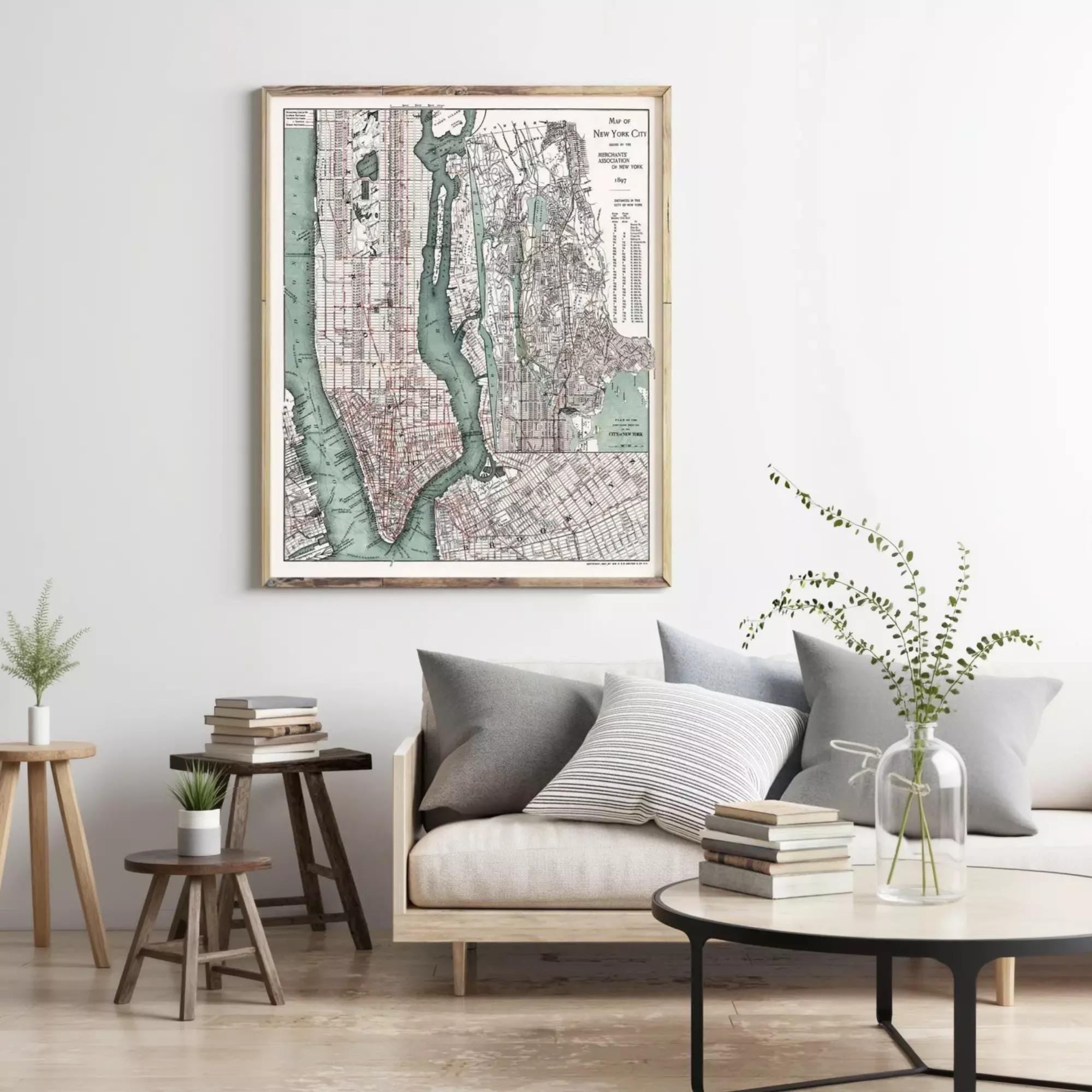 a living room with a large framed map of New York City hanging on the wall above a couch with pillows. The room also includes a coffee table with books and a vase of greenery, creating a cozy and inviting atmosphere.