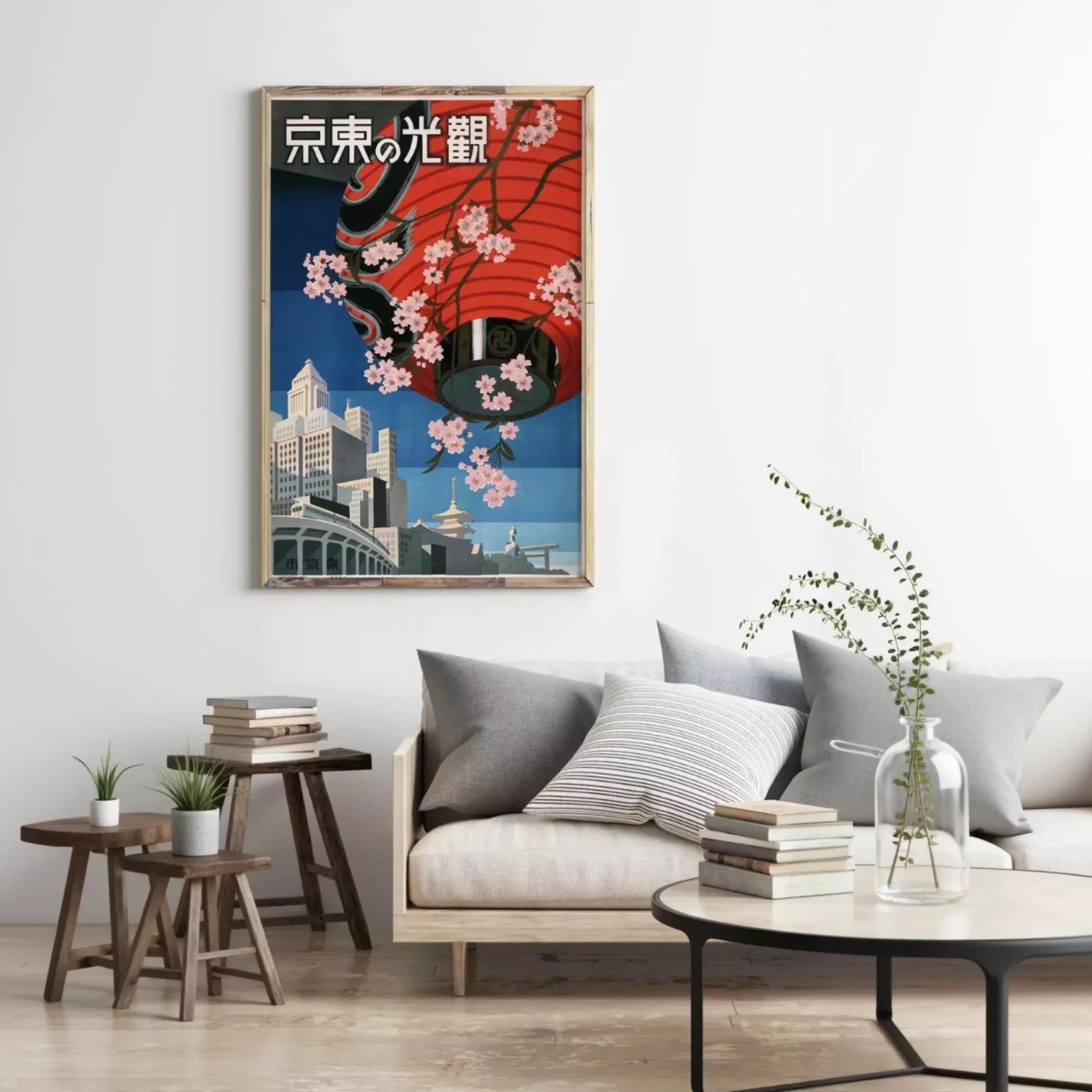 a living room with a large framed poster of a cityscape hanging on the wall, a gray sofa with a stack of books, and a small table with a plant.