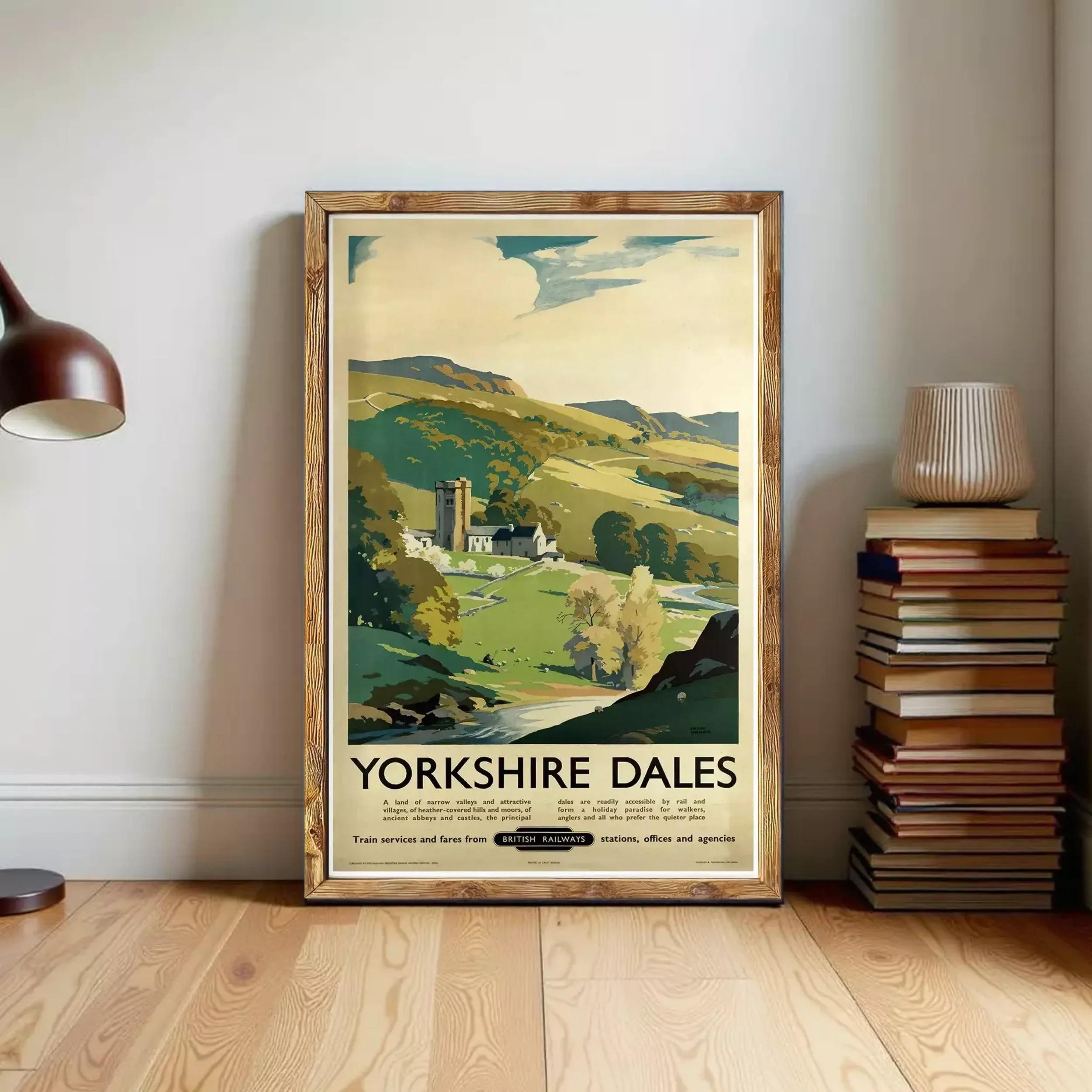 A framed vintage poster of Yorkshire Dales, a scenic countryside in Yorkshire, England, is displayed on a wall next to a stack of books and a lamp.