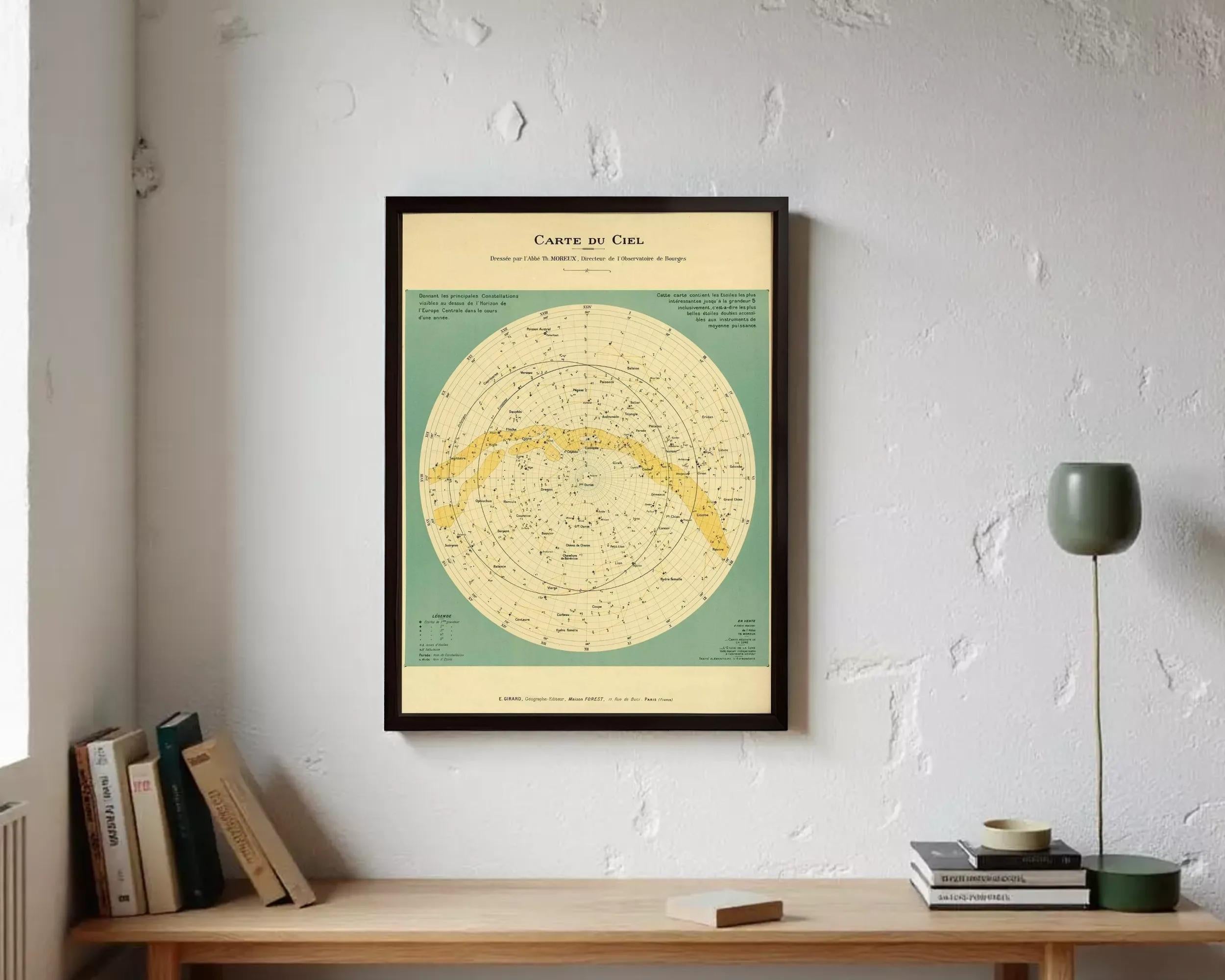 a framed vintage-style map of the night sky, hanging on a wall above a wooden desk with books and a lamp.