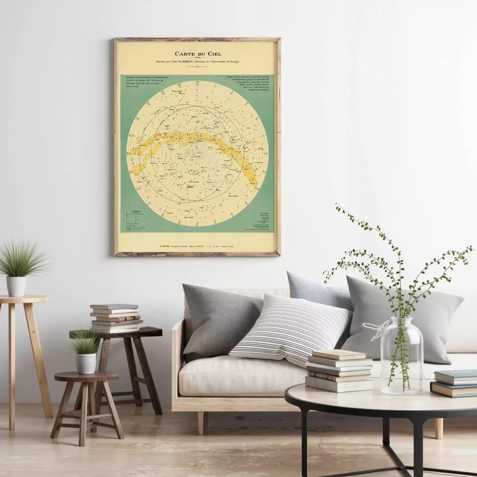 a living room with a framed vintage-style map of the night sky hanging on the wall above a couch with pillows. The room also includes a coffee table with books and a vase of greenery, creating a cozy and inviting atmosphere.