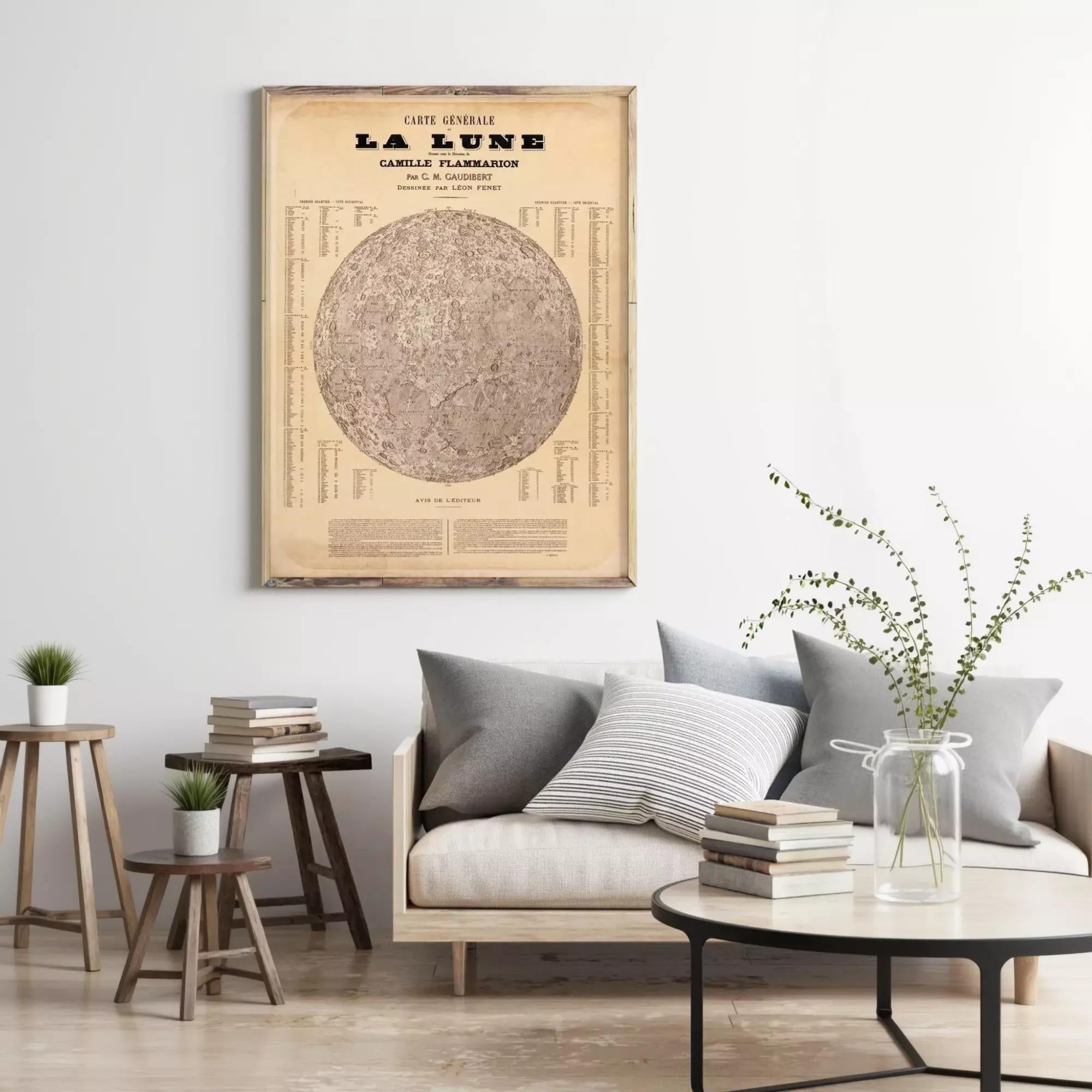 a living room with a framed vintage map of the moon hanging on the wall above a couch with pillows. There are also some books and a vase with greenery on the couch.