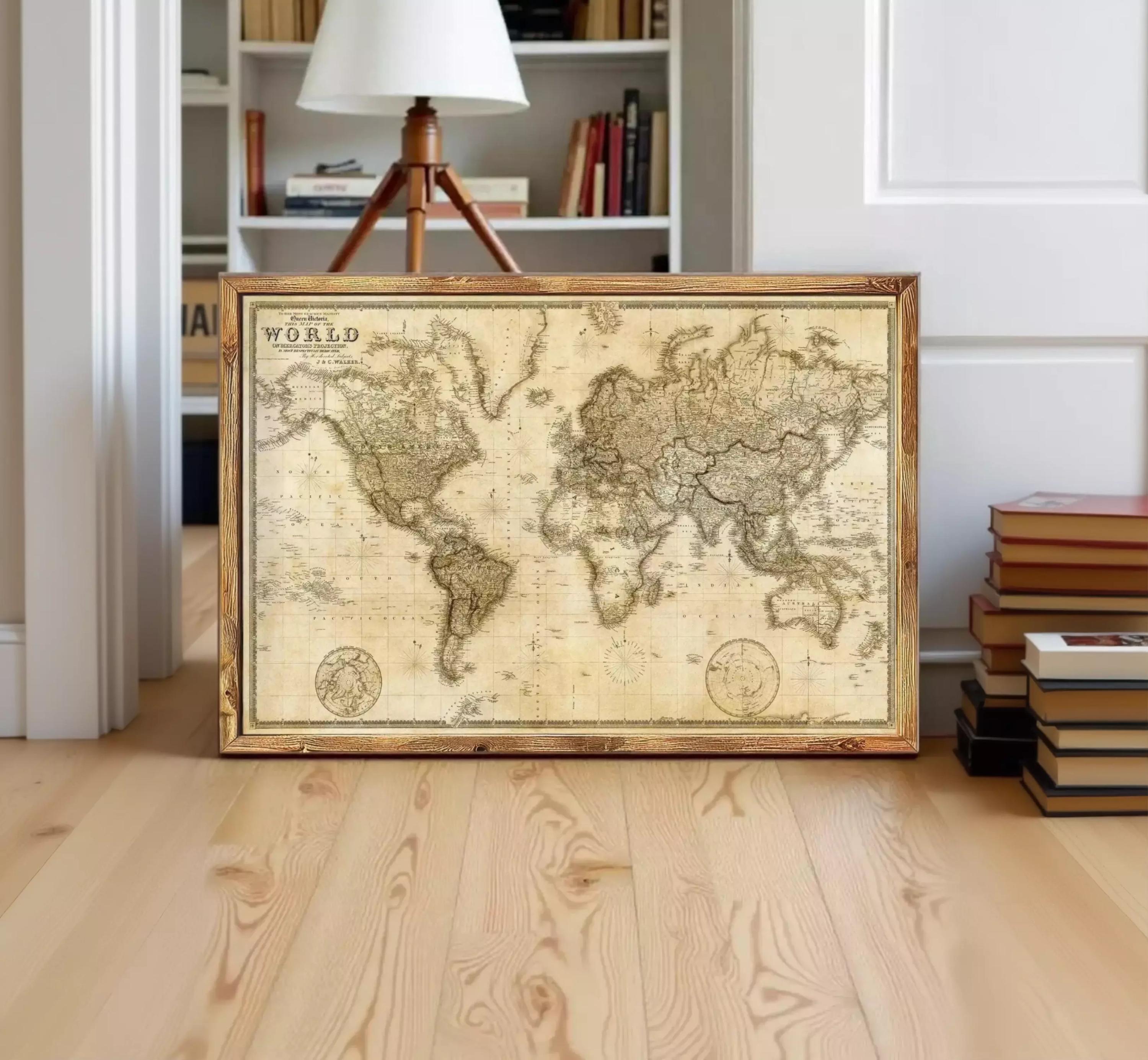 A framed antique world map is displayed on a wooden floor in a room with a bookshelf in the background.