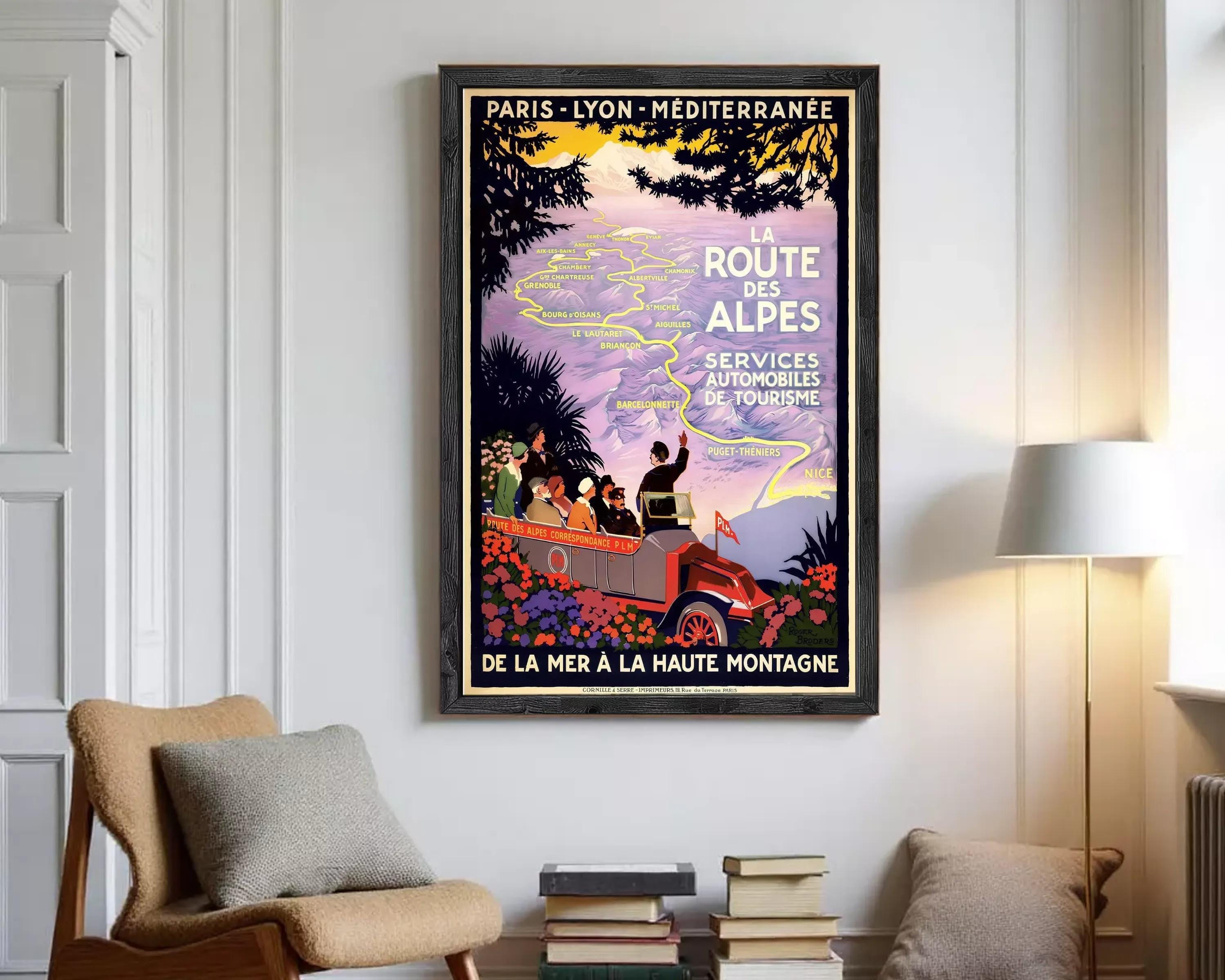 A framed vintage travel poster advertising a tour of the route to the Alps, featuring a car and people traveling through a scenic landscape.