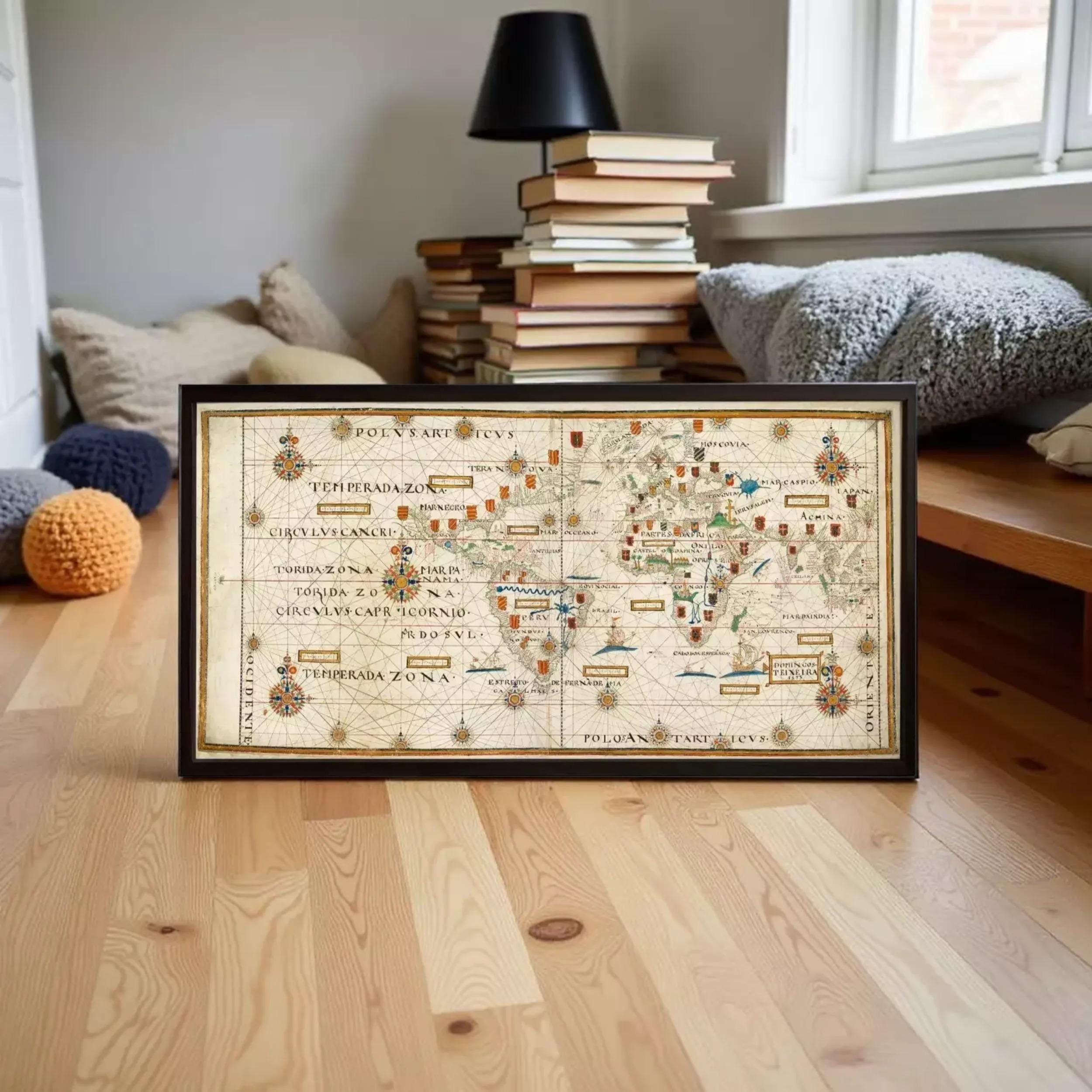 A framed map of the world is displayed on a wooden floor in a room with books and pillows in the background.
